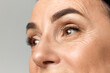 Cropped portarit of beautiful middle-aged woman with healthy, natural condition skin looking away over grey studio background.
