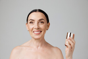 Beautiful old age. Photo of elderly smiling woman holding bottle over grey studio background. Well-kept old lady