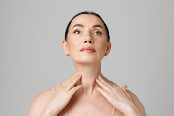 double chin treatment. elderly woman touching skin on neck over light grey background. copy space fo