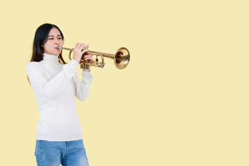 A pretty and talented Asian woman is playing the trumpet, isolated yellow background