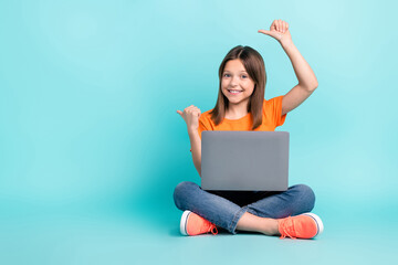 Photo of funny charming preteen age girl sitting floor advertsise modern technology empty space isolated on cyan color background
