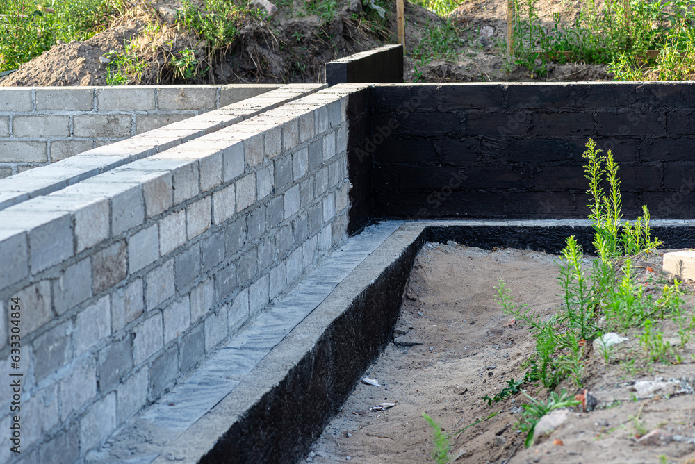 Footings made of concrete blocks painted with black dispersion asphalt-rubber mass, reinforced concrete pillars visible.