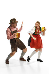 Wall Mural - Two celebrating friends. Full lenght portrait of emotional man and woman wearing folk festival outfits, having glasses with Bavarian beer.