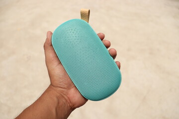 A Teal colour Wireless handy pocket speaker held in a Hand diagonally in an isolated background 