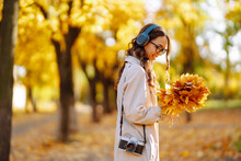Smiling Woman With Retro Camera And Headphones Enjoys Sunny Weather In Autumn Park. Autumn Lifestyle.