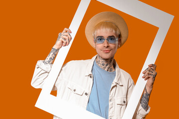 Wall Mural - Young tattooed man in stylish sunglasses with frame on color background