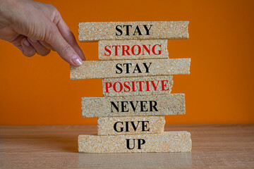 Brick blocks with concept words Stay strong stay positive never give up. Beautiful orange background. Copy space. Businessman hand. Motivational business never give up concept.