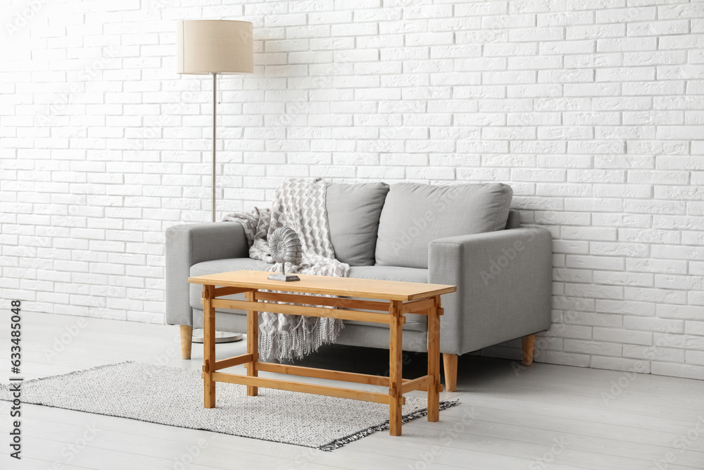 Light wooden coffee table with couch and floor lamp near white brick wall