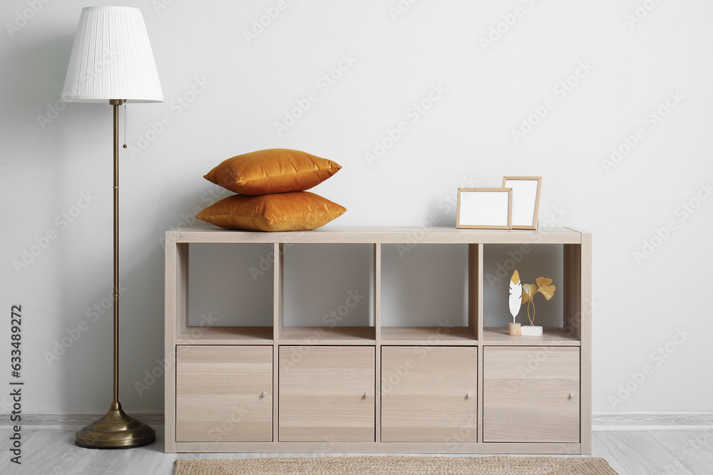 Wooden cabinet with cushions and blank frames near white wall