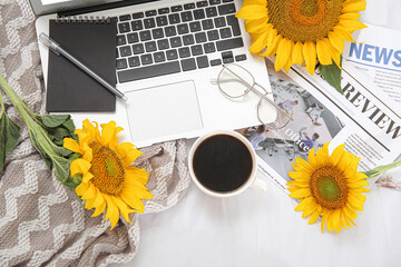 Sticker - Beautiful sunflowers, cup of coffee, eyeglasses, newspapers and modern laptop on light fabric background