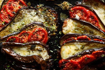 Wall Mural - Close-up view of stuffed roasted eggplants with tomatoes and cheese seasoned herbs on a black background