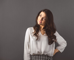 Wall Mural - Beautiful happy smiling woman with long brown curly healthy hair looking up and dreaming about in white shirt, formal clothing. Closeup studio