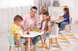 © New Africa - Nursery teacher and group of cute little children playing at desks in kindergarten. Activities for motor skills development