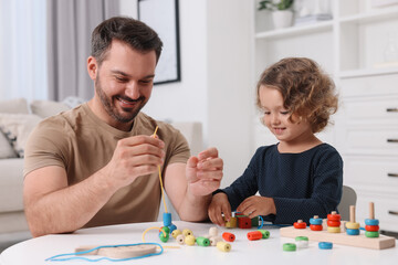 Poster - Motor skills development. Father and daughter playing with wooden pieces and strings for threading activity at table indoors