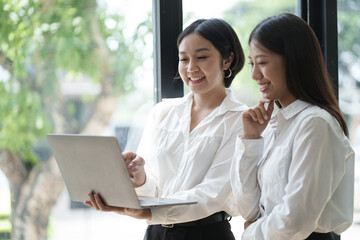 Wall Mural - Two professional smart Asian business woman working together in the office room, discussion information from laptop.