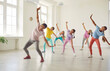 © Studio Romantic - Smiling friendly choreographer showing her students girls dance exercises in studio. Happy children training in a group choreography class doing dance workout and learning modern dances.