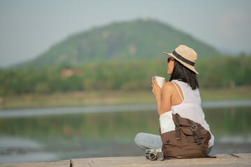 Wall Mural - asian woman traveler with backpack and cup of coffee sitting on quayside relax during coffee break on background summer vacations and lifestyle hiking concept.