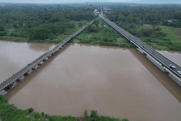 Aerial view of the long bridge over the brown watery river. the river delta is overgrown with green weeds. jembatan kali Progo. 