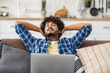 © kucherav - Happy young man freelancer or student with his hands on his head and his eyes closed relaxing on sofa at home