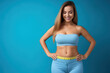 Fit woman with measuring tape, Diet and weight loss concept, perfect body. Beautiful woman measuring her waist with a measure tape on blue background copy space