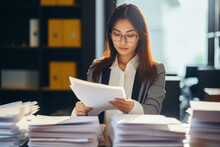 Young Busy Asian Business Woman Lawyer, Tax Accountant Manager Holding Paper Documents Checking Bills, Doing Sales Invoice Accounting, Reading Legal Contract Or Bank Statement Sitting At Desk