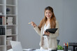 © amnaj - Smiling young happy Asian businesswoman working with laptop and documents in office. Accountant or beautiful asian female worker working happily in the office.