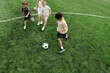 © pressmaster - Above angle of several schoolchildren playing soccer on green football field at stadium while three of them running after ball during game