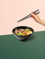 Photo of Japanese ramen soup with chopsticks and hand on the background.