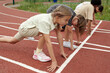 © pressmaster - Side view of youthful intercultural schoolkids in activewear standing on tracks by start line at stadium while taking part in running competition