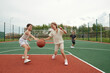 © pressmaster - Two cute blond schoolgirls in activewear dribbling ball while running along field or stadium towards basket on background of their classmate