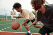 © pressmaster - African American schoolboy in activewear dribbling ball while running forwards in front of his classmate while blond girl standing on background