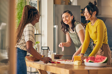 Friends, smile and women cooking pizza in kitchen, bonding and having fun together in home. Happy, girls and baking food, margherita and salami bread at lunch, cheese on meat and brunch in house