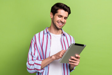 Fototapete - Photo of pleasant intelligent cheerful man with stubble dressed striped shirt look at tablet read email isolated on green color background