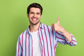 Poster - Portrait of pleasant optimistic man with brunet hair wear stylish clothes showing thumb up good job isolated on green color background