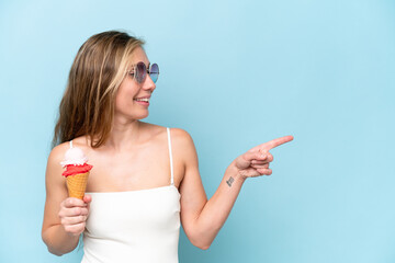 Wall Mural - Young blonde woman in swimsuit holding an ice cream isolated on blue background pointing to the side to present a product