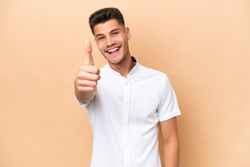 Wall Mural - Young caucasian man isolated on beige background with thumbs up because something good has happened