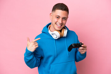 Wall Mural - Young brazilian man playing with a video game controller isolated on pink background giving a thumbs up gesture