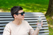 woman with sunglasses drinks water from bottle on hot summer day, sitting on a bench in the park