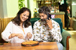 © PRASANNAPIX - Indian man sitting with his wife at restaurant and talking on smartphone.