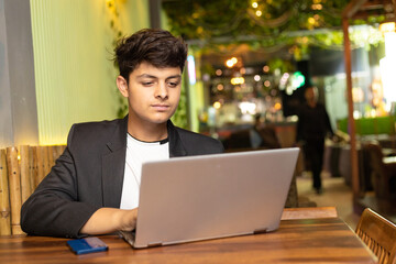 Wall Mural - Young indian boy using laptop at restaurant