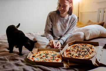 two pizzas at home in a cozy bed of a woman and a cat.