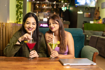 Poster - Two indian female friends enjoying cold drinks together at restaurant.