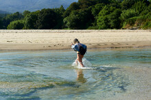 A Woman With A Backpack, Pulls Up Her Dress To The Height Of Her Bikini To Wade Through The Waters Of The Cans River At Its Mouth On Aguieira Beach