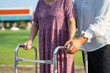 Caregiver help Asian elderly woman patient walk with walker in park, healthy strong medical concept.