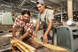 Two young carpenters working with wood standing at table in workshop