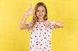 blonde kid girl wearing polka dot shirt over yellow studio background showing thumbs up and thumbs down, difficult choose concept