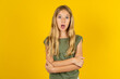 Shocked embarrassed blonde kid girl wearing green T-shirt over yellow studio background keeps mouth widely opened. Hears unbelievable novelty stares in stupor