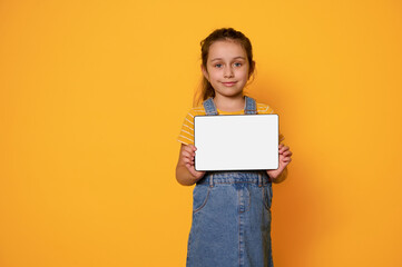 Adorable child girl showing digital tablet with white empty blank screen, smiling looking at camera, isolated background