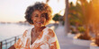 © Elena - Lifestyle portrait of happy mature black woman with curly hair on tropical vacation standing on boardwalk