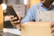 © Kritdanai - Asian male small business owner using mobile app on smartphone checking parcel box. Warehouse worker, seller holding phone scanning retail dropshipping package postal parcel bar code.